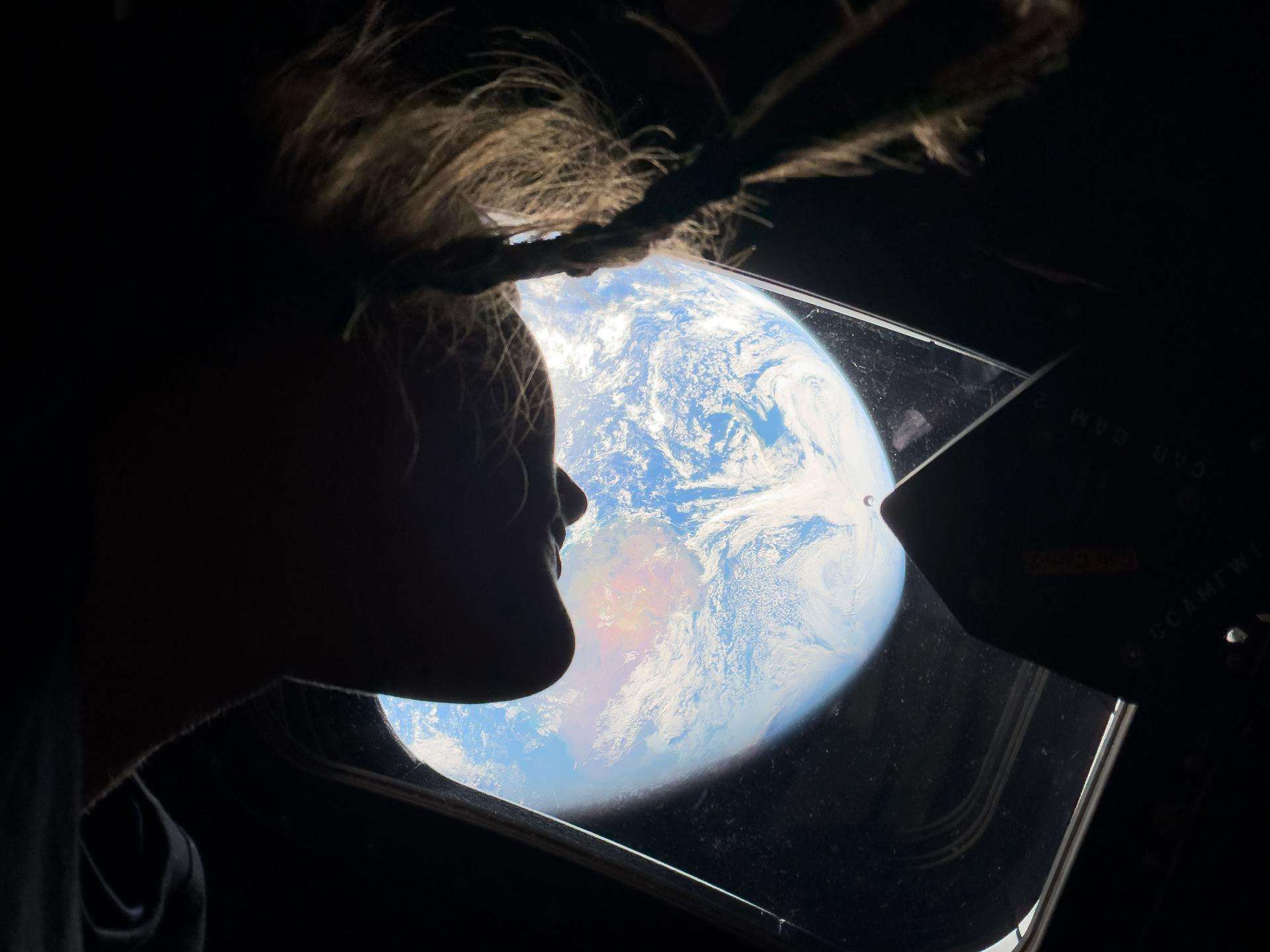 An Artemis II astronaut gazes at Earth through the Orion capsule window