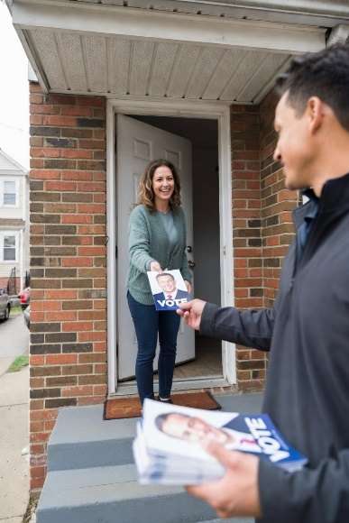 A campaign volunteer hands literature to a voter at her door